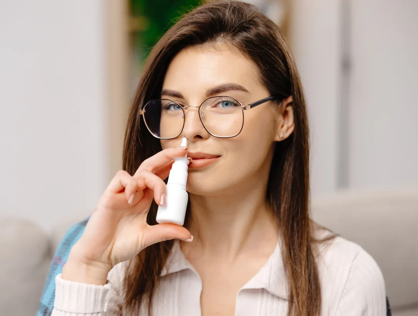 Woman wearing glasses using a nasal spray inhaler